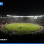 A brightly lit cricket stadium at night during a Twenty20 match with a packed audience.