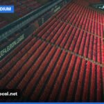 An empty football stadium with red seats, ready for a match under clear skies.