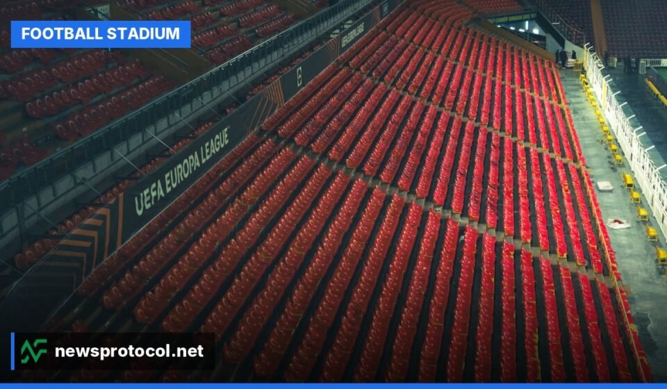 An empty football stadium with red seats, ready for a match under clear skies.